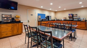 A hotel dining area with a large table, chairs, a kitchen area, and a television mounted on the wall. - Best Western San Diego Pacific Beach/mission Bay (San Diego)