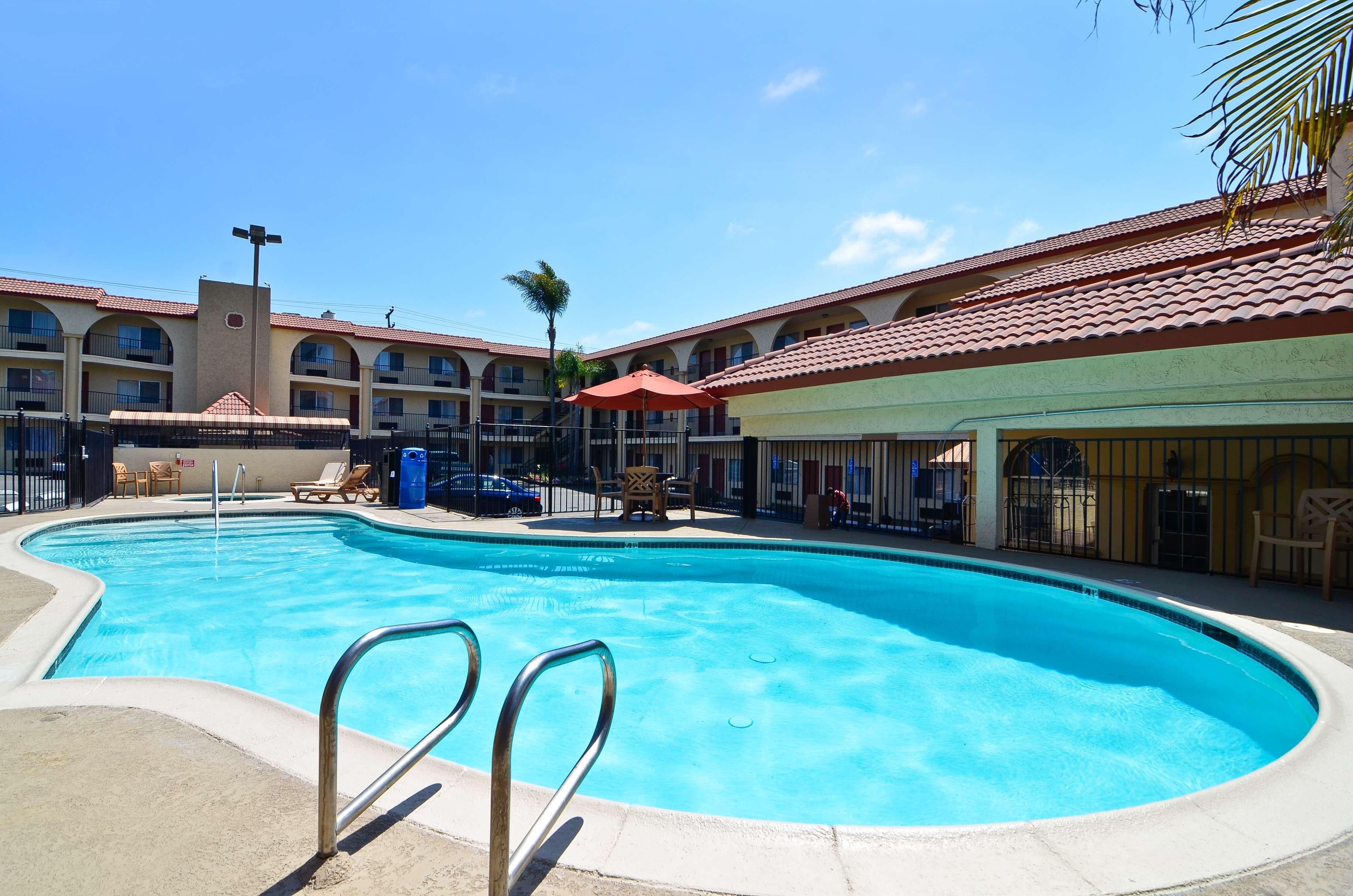 A swimming pool with a clear blue water, surrounded by a building with a red-tiled roof and multiple balconies.