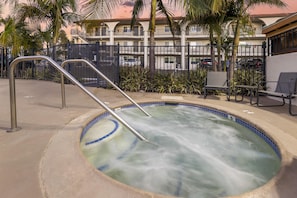 A hot tub with metal railings, surrounded by a concrete deck, palm trees, and a building with balconies in the background. - Best Western San Diego Pacific Beach/mission Bay (San Diego)