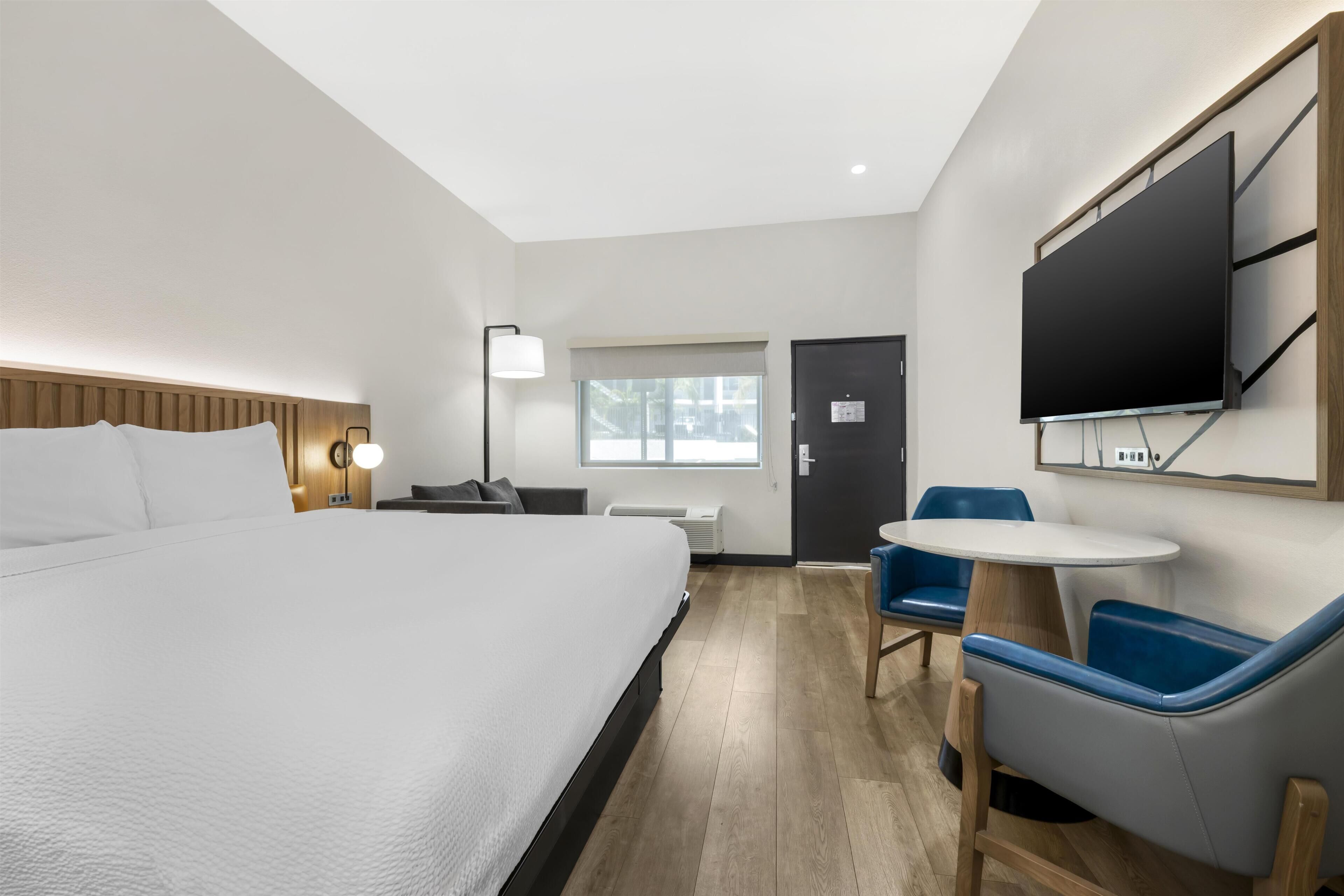 Ein Hotelzimmer mit einem großen Bett, einem Schreibtisch, einem Stuhl, einem Fernseher und einem Fenster.