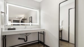 A modern bathroom with a white sink, a large mirror with integrated lighting, a black pipe under the sink, and a wooden floor. - Best Western San Diego Pacific Beach/mission Bay (San Diego)