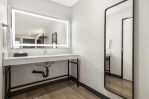 A modern bathroom with a white sink, a large mirror with integrated lighting, a black pipe under the sink, and a wooden floor. - Best Western San Diego Pacific Beach/mission Bay (San Diego)