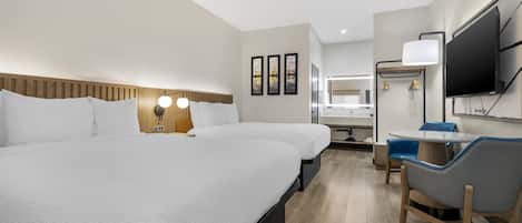 A hotel room with a large bed, a desk with a chair, a TV, and a bathroom visible in the background.