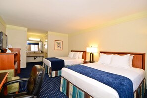 A hotel room with two beds, a desk, a chair, a mirror, a lamp, and a bathroom visible through an open door.
