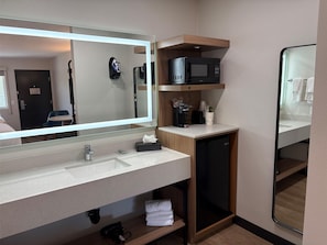Un baño moderno con un espejo grande, un lavabo, un microondas y un estante pequeño con artículos de tocador.