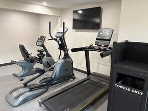 A gym with two elliptical machines, a treadmill, and a TV mounted on the wall.