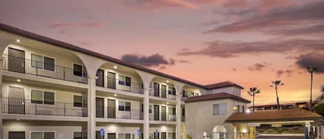 A multi-story hotel with balconies, a parking lot, and a clear sky.