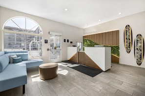 A modern reception area with a large arched window, a reception desk, a blue sofa, and a round wooden table. - Best Western San Diego Pacific Beach/mission Bay (San Diego)