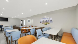 A modern dining area with tables and chairs, a flat-screen TV mounted on the wall, and a cityscape artwork. - Best Western San Diego Pacific Beach/mission Bay (San Diego)