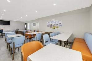 A modern dining area with tables and chairs, a flat-screen TV mounted on the wall, and a cityscape artwork. - Best Western San Diego Pacific Beach/mission Bay (San Diego)
