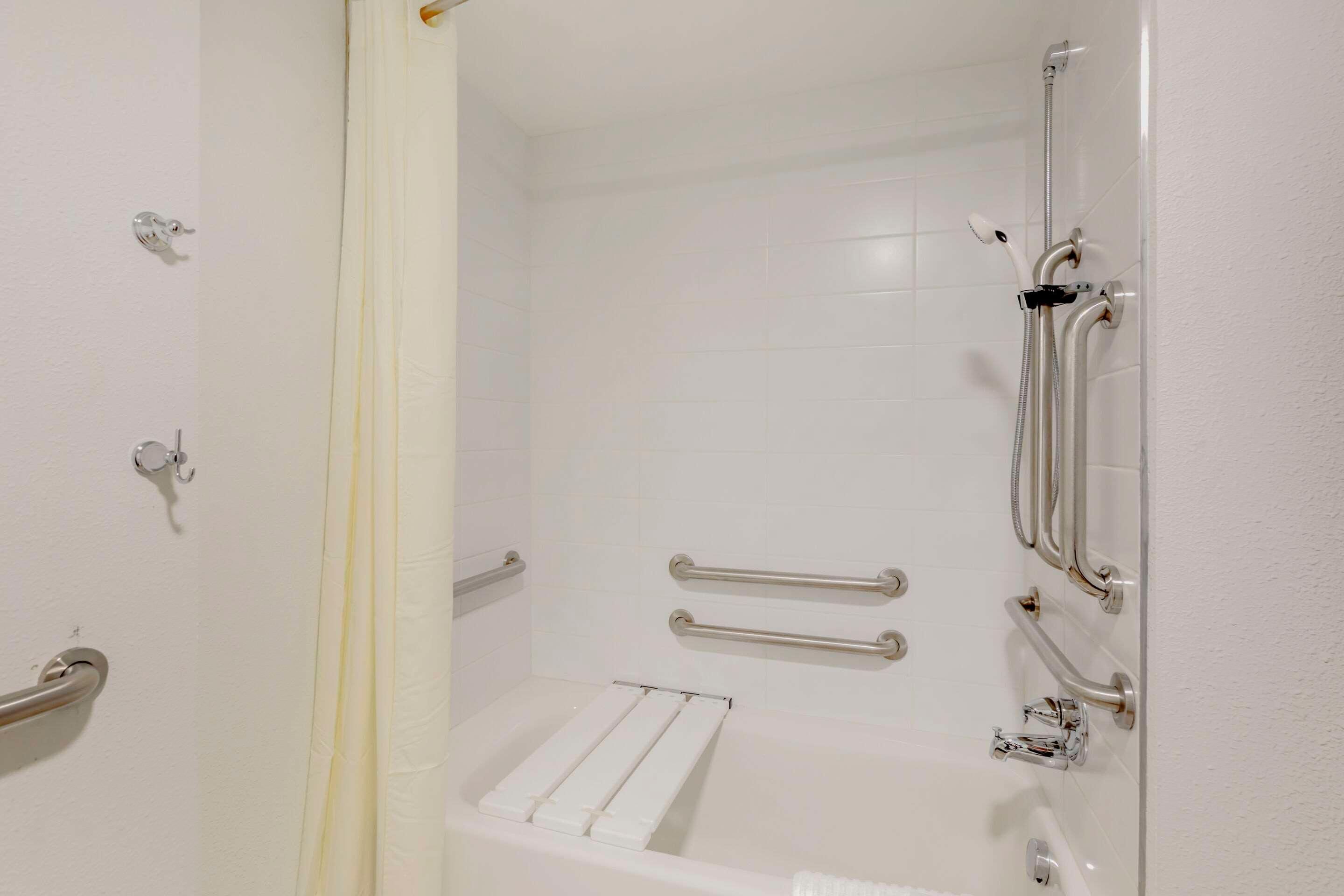 Une salle de bain avec une baignoire blanche, des barres d’appui et un espace douche.
