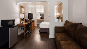 Une chambre d’hôtel compacte comprenant un coin cuisine, un lit, un canapé marron et un bureau avec une télévision.