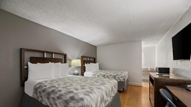A hotel room with two beds, a desk, a chair, and a television. - Americas Best Value Inn Orlando (Orlando)