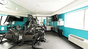Une salle de sport équipée de matériel d’exercice, d’un miroir, d’une horloge et d’une fenêtre avec des stores.