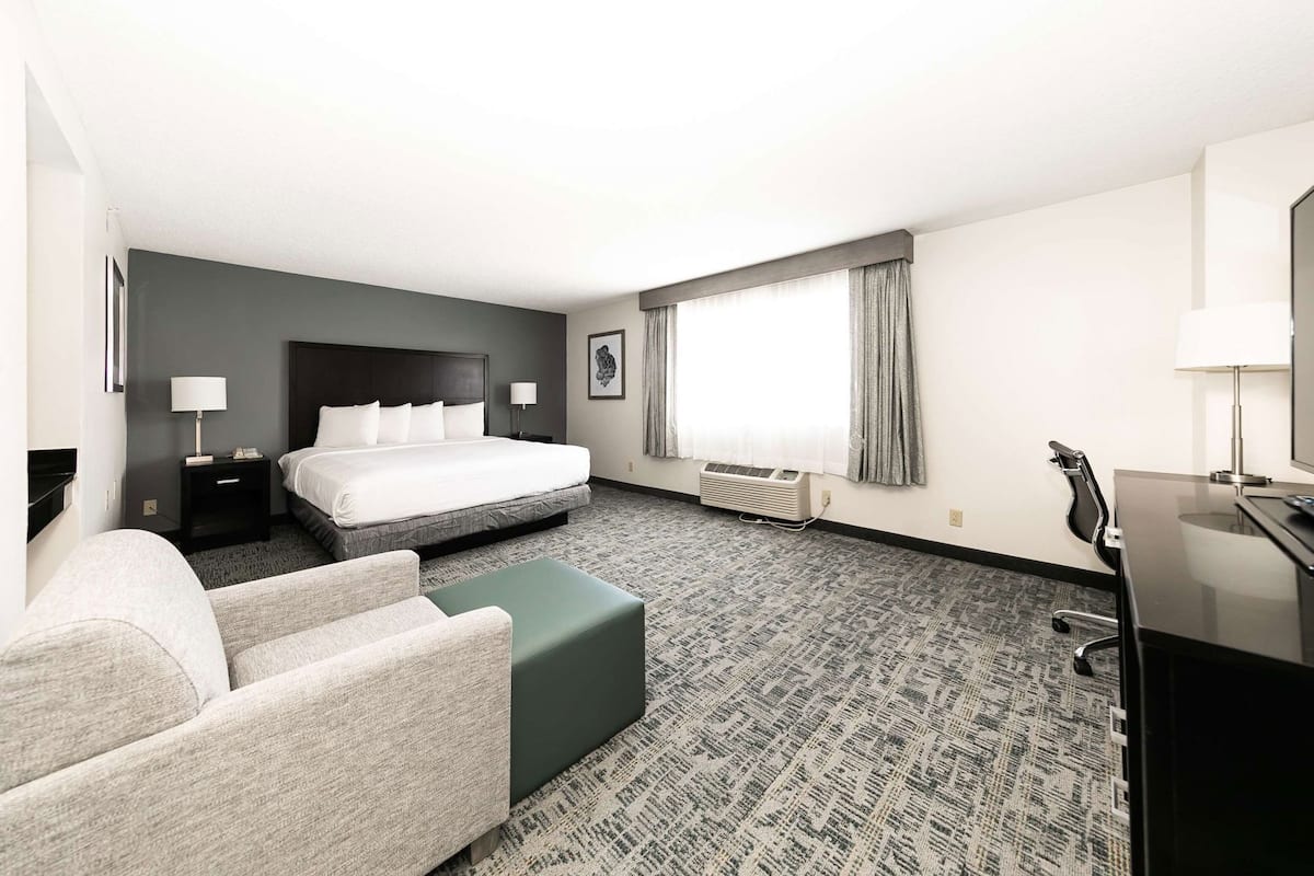 Ein Hotelzimmer mit Bett, Schreibtisch, Stuhl, Sofa und einem großen Fenster mit Vorhängen.