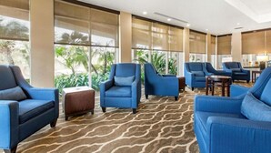 A hotel lobby with blue armchairs, a patterned carpet, and large windows with views of greenery. - Best Western Inn & Suites San Diego - Zoo/seaworld Area (San Diego)