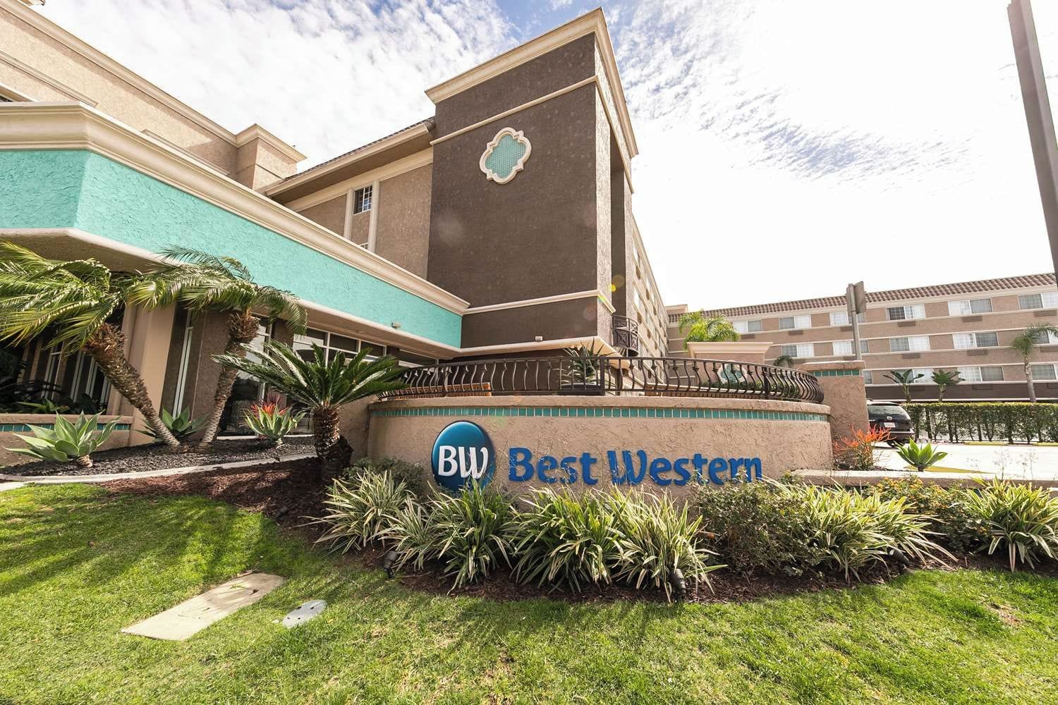 Un hôtel avec une enseigne indiquant « Best Western » et une entrée aménagée avec des palmiers.
