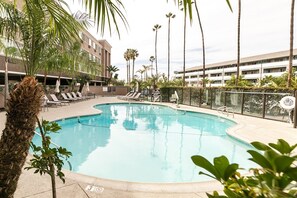 Une piscine avec des chaises longues, des palmiers et un bâtiment en arrière-plan.