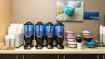 A juice bar with multiple dispensers, a sign for Hydrate Juice Bar, and a variety of food and drink containers.