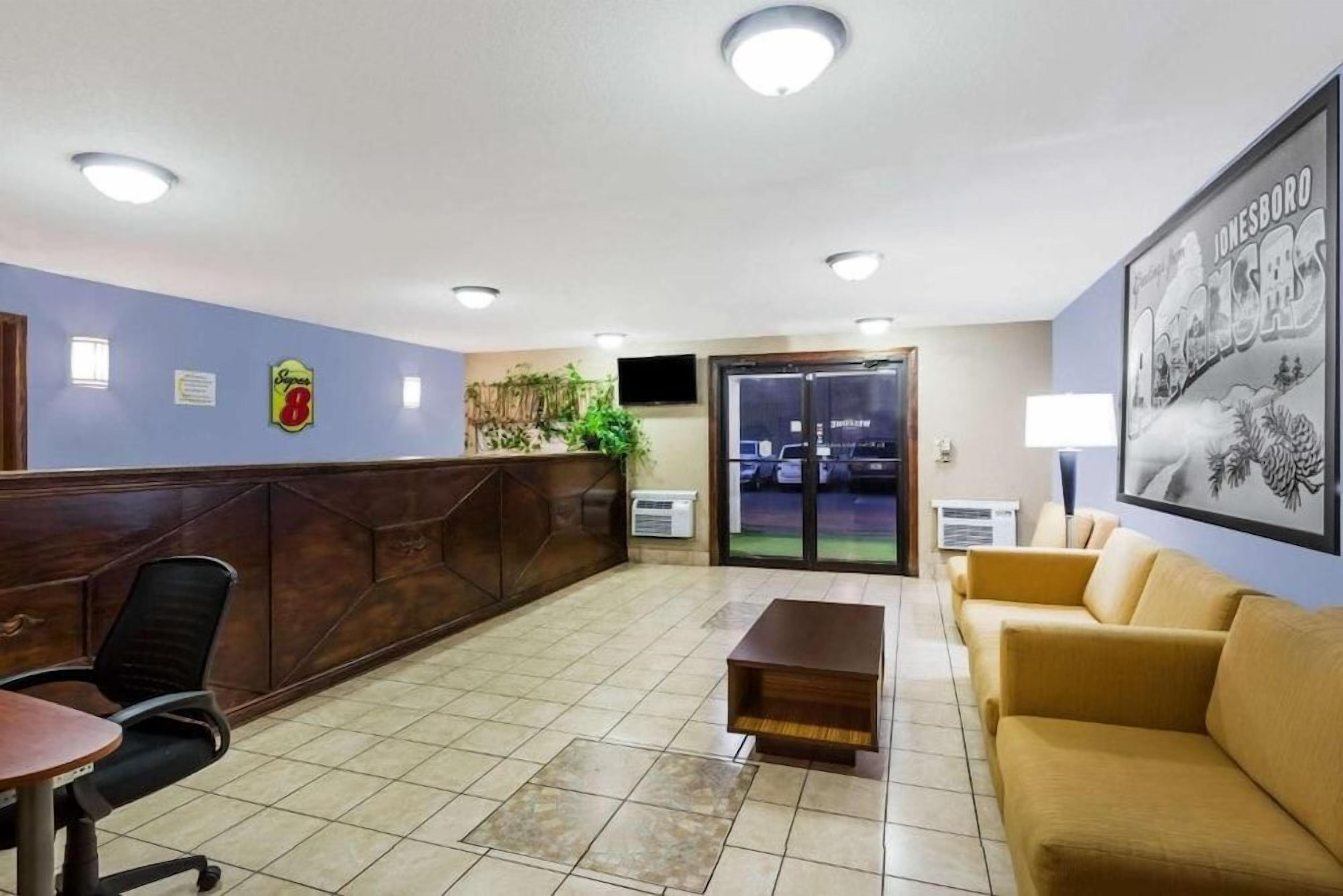 A reception area with a wooden reception desk, a seating area with a sofa and chairs, a tiled floor, and a framed picture on the wall.