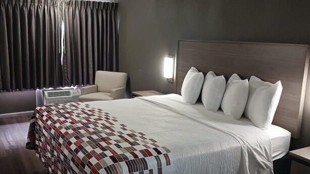 Une chambre d’hôtel avec un grand lit, une chaise, un bureau et une fenêtre avec des rideaux.