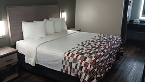 Un lit bien fait, avec une couverture, une table de chevet dotée d’un tiroir et une lampe fixée au mur.