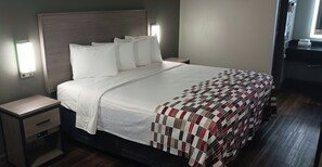 A neatly made bed with a quilt, a bedside table with a drawer, and a wall-mounted light. - Red Roof Inn Fort Worth West (Fort Worth)