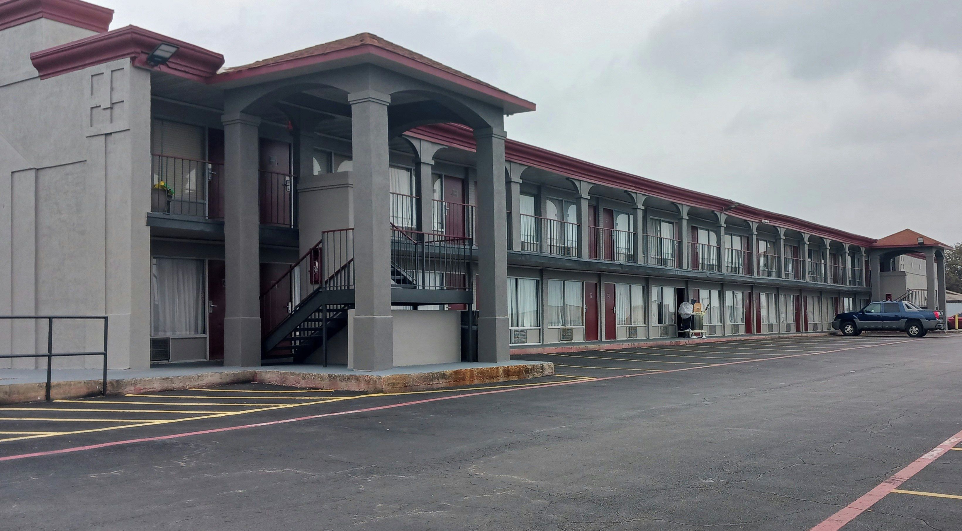 Un motel con una hilera de habitaciones, un corredor cubierto y un estacionamiento.