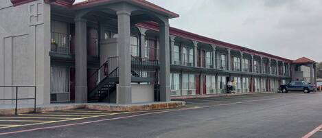 Un motel con una hilera de habitaciones, un corredor cubierto y un estacionamiento.