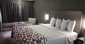 A hotel room with a large bed, a chair, a bedside table, and a window with curtains. - Red Roof Inn Fort Worth West (Fort Worth)