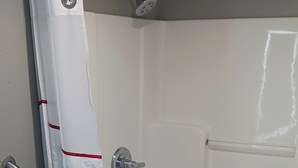 Une cabine de douche avec un rideau blanc, une barre d’appui et des toilettes dans la pièce adjacente.