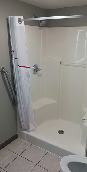 A shower stall with a white curtain, a grab bar, and a toilet in the adjacent room. - Red Roof Inn Fort Worth West (Fort Worth)