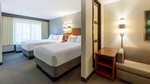 Une chambre d’hôtel avec deux lits, un canapé, une table de chevet et une lampe.