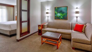 Une chambre d’hôtel comprenant un lit, un canapé, un pouf et deux lampes fixées au mur.