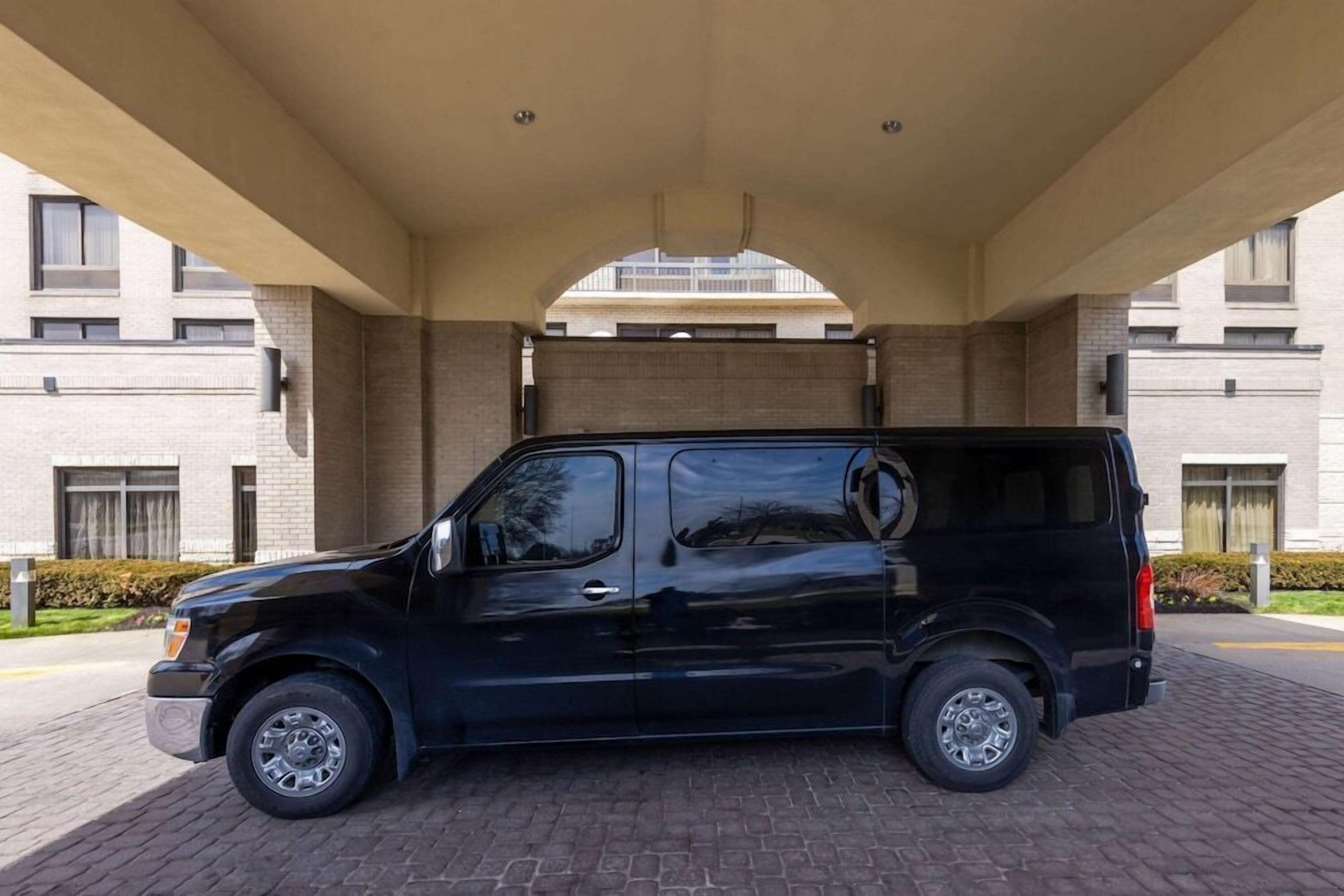 A black van parked under a covered area with a modern building in the background.