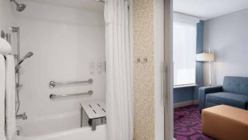 A hotel bathroom with a bathtub, shower, and grab bars.