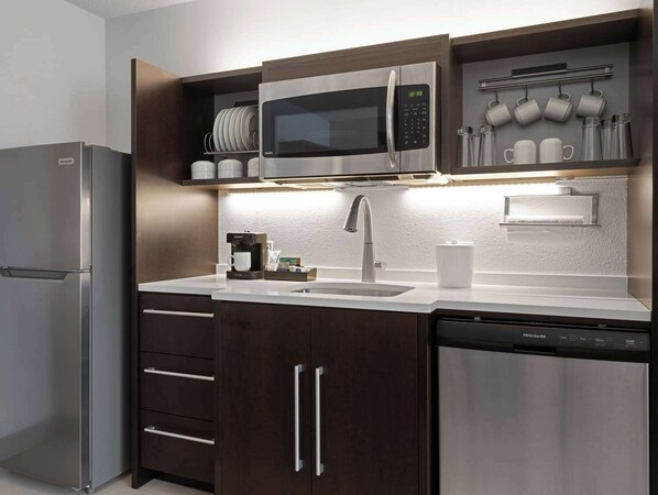 A modern kitchen with a stainless steel refrigerator, a built-in microwave, a coffee maker, and a dishwasher. - Home2 Suites by Hilton Indianapolis Keystone Crossing (Indianapolis)