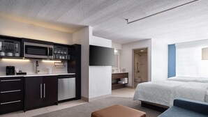 Una habitación de hotel moderna con kitchenette, una cama, un sofá y zona de ducha.