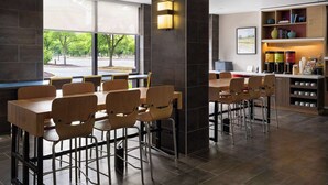 Un comedor moderno con mesas y sillas de madera, una estación de café y vistas al exterior.