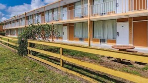 Een meerhoog motel met een gele gevel, balkons en een gazon met houten omheining.