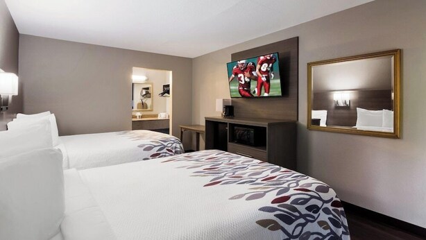 Een hotelkamer met twee bedden, een televisie, een spiegel en een klein bureau met lamp.