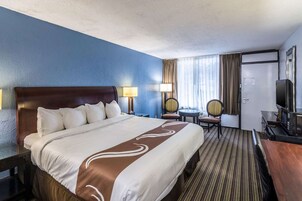 Habitación de hotel con una cama grande, dos mesitas de noche, un escritorio con silla, televisión y ventana con cortinas.