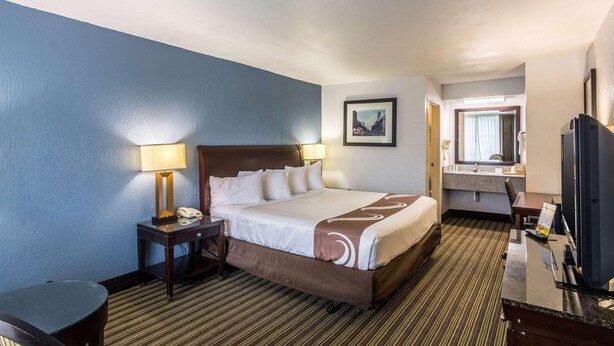 A hotel room with a bed, bedside tables, a desk, a chair, a television, and a bathroom visible through an open door. - Rest and Relax Inn (Pensacola)