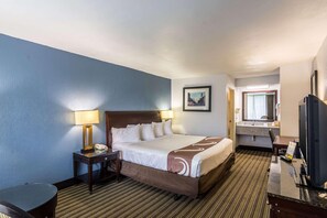Ein Hotelzimmer mit Bett, Nachttischen, Schreibtisch, Stuhl, Fernseher und einem durchgehenden Türrahmen einsehbarer Badezimmers.