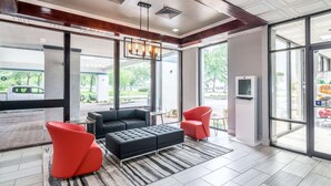 A modern lobby with a black sofa, red chairs, a patterned rug, and large windows offering a view of the outside. - Rest and Relax Inn (Pensacola)