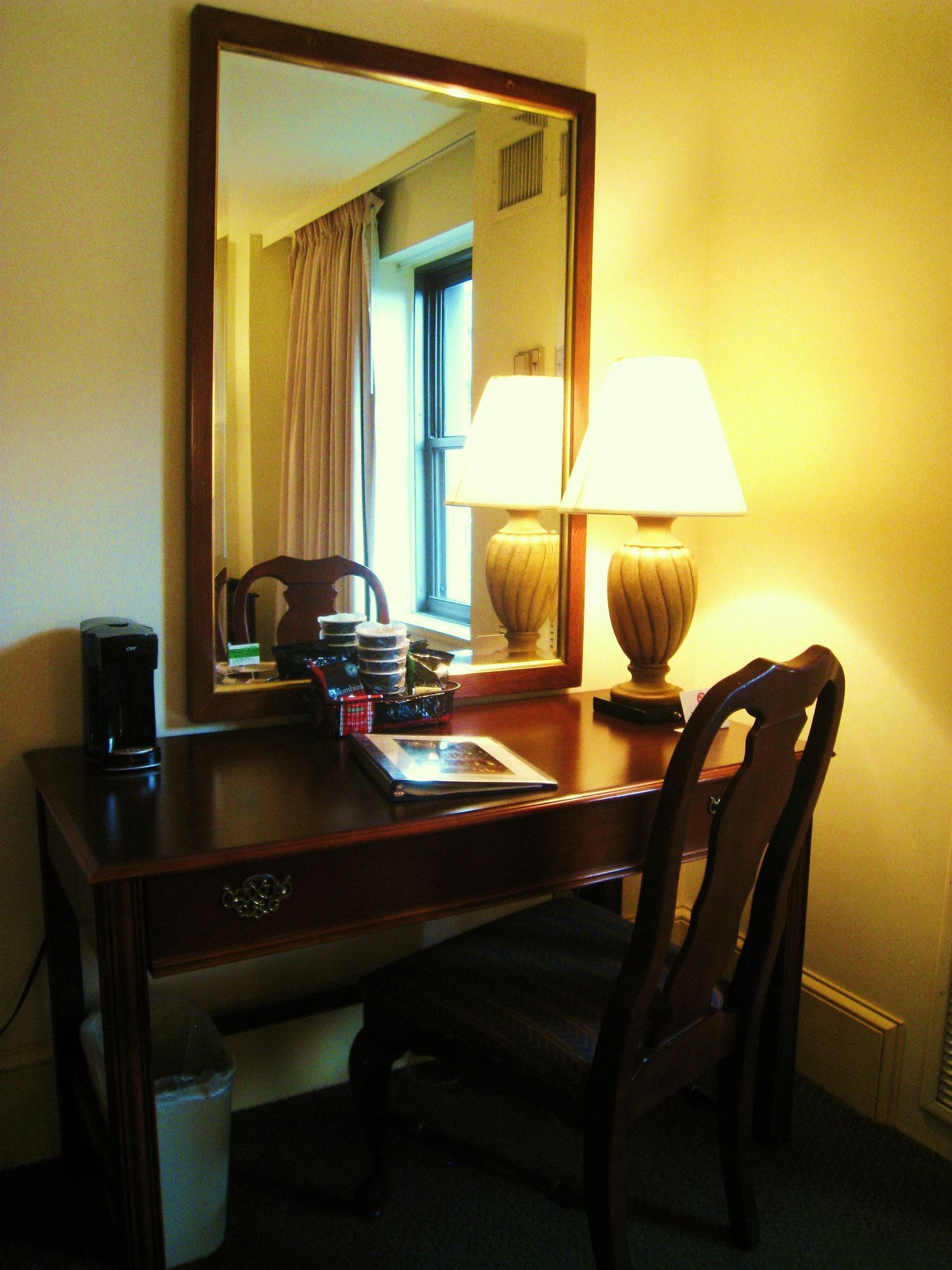 Ein Hotelzimmer mit Schreibtisch, Lampe, Kaffeemaschine und Stuhl.