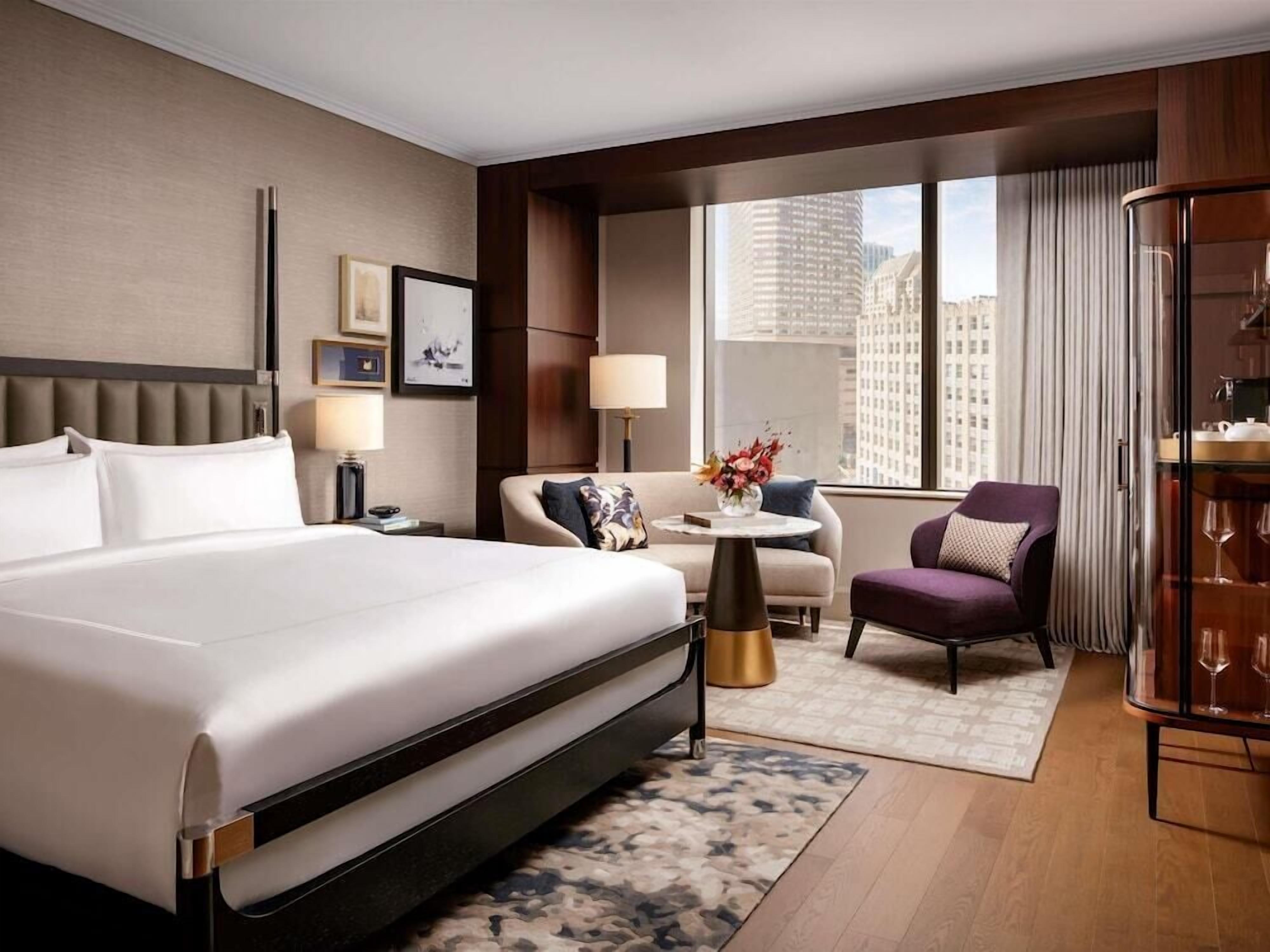 A hotel room with a large bed, a sofa, a chair, a small table, and a glass cabinet.