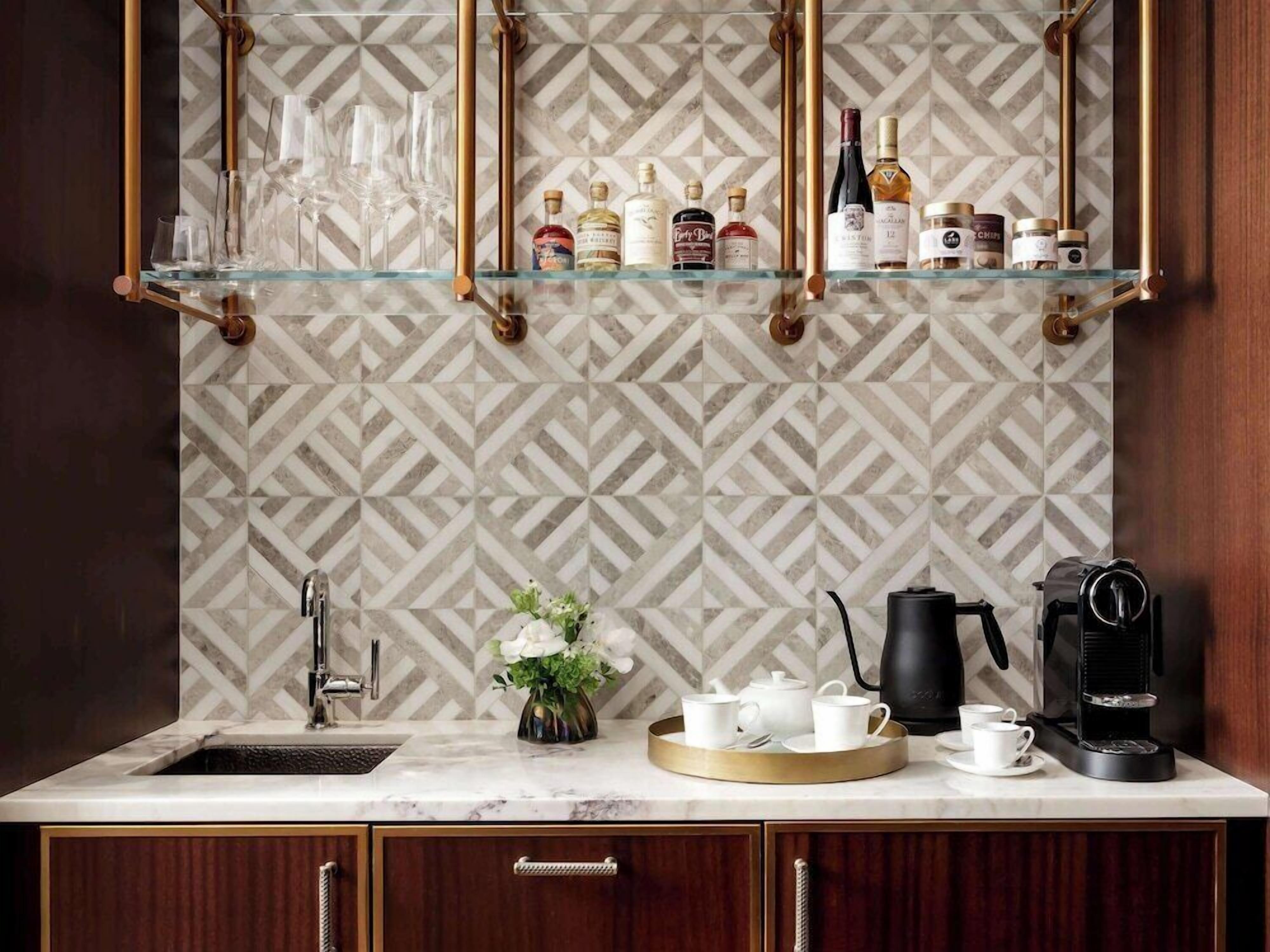 A kitchen with a marble countertop, a coffee maker, a tea pot, and a glass shelf above the sink holding various bottles.