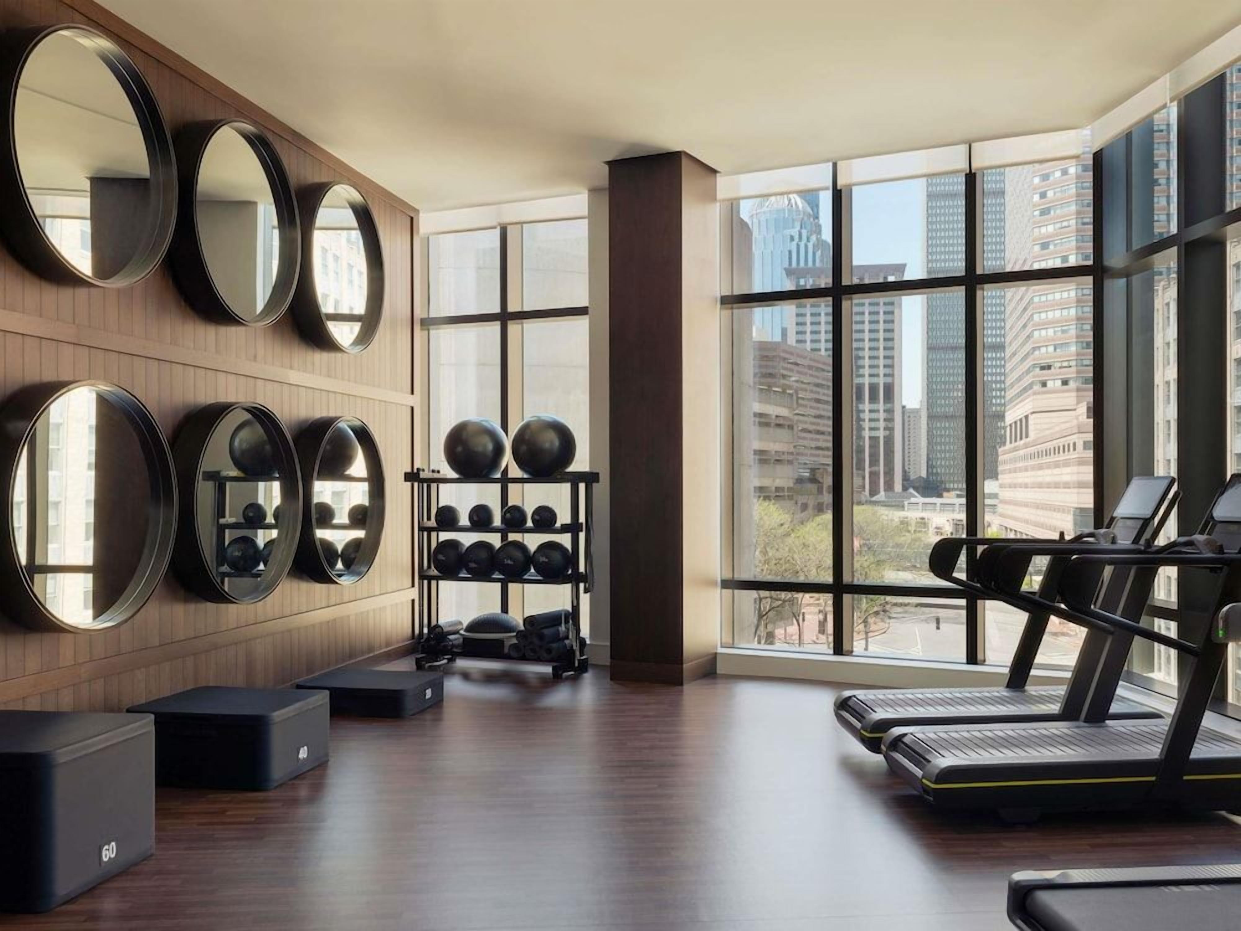 A gym with exercise equipment, large mirrors, and a view of the city through large windows.