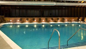 En inomhuspool med kristallklart blått vatten, omgiven av trädäck med solstolar och bekväma sittplatser.